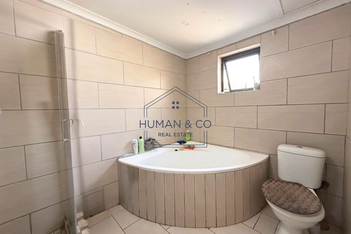 A functional bathroom featuring a corner bathtub, a separate shower enclosure, and a standard toilet with neutral wall and floor tiling.