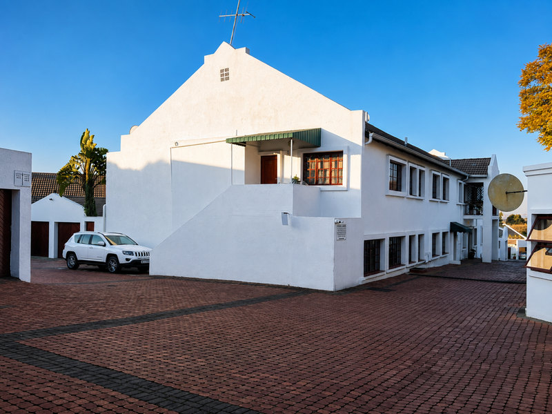 Exterior view of a white apartment building featuring a gabled roof, paved driveway, and external staircase access.