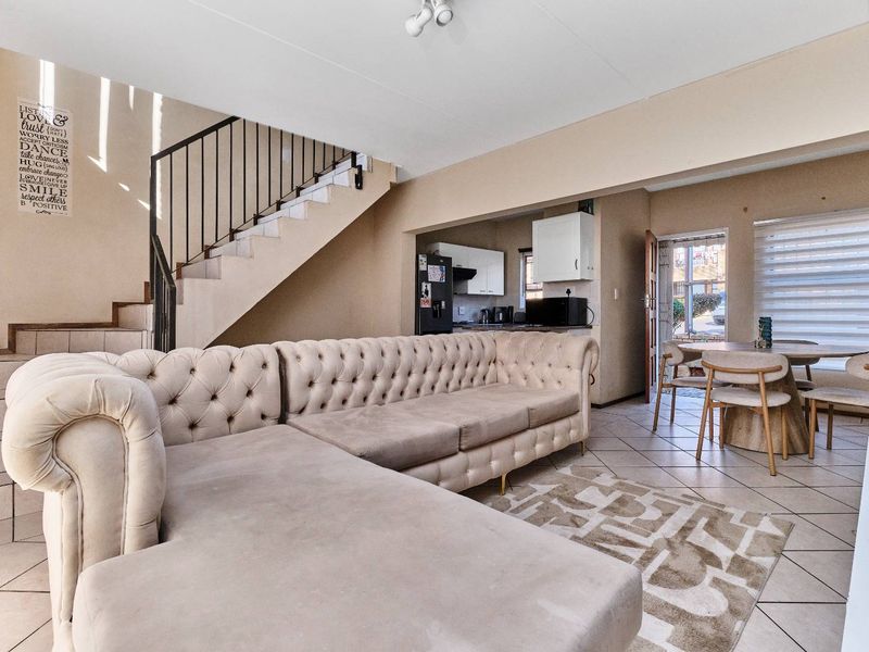 Open-plan living and dining area featuring tiled floors, a staircase with metal balustrade, and an adjoining kitchen space with direct exterior access.