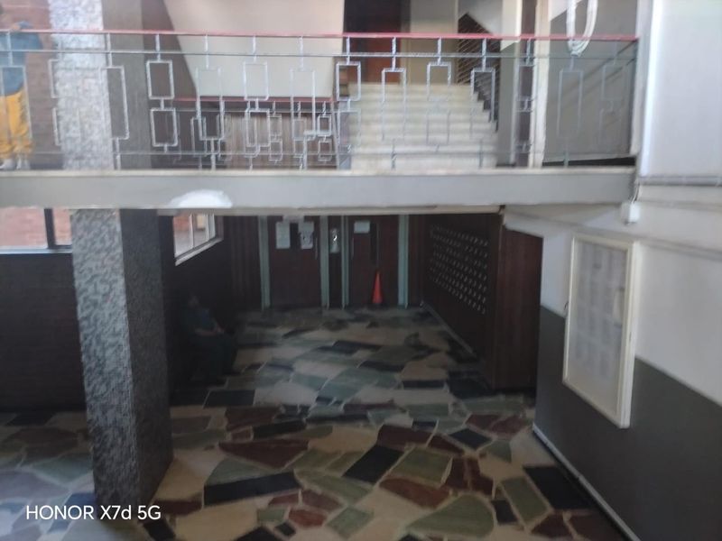 A communal apartment building entrance lobby featuring stone tile flooring, a metal balustrade, and a staircase leading to upper levels.