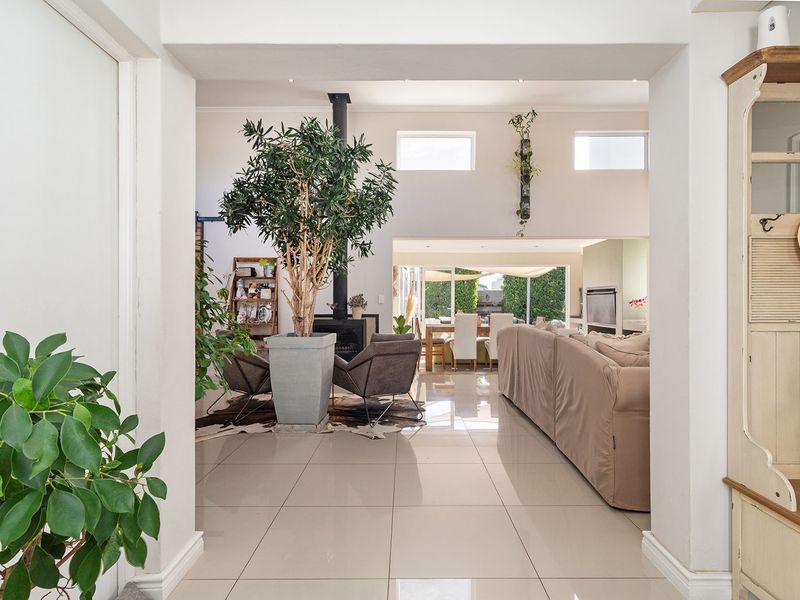 Spacious open-plan living area featuring high ceilings, large format floor tiles, a modern fireplace, and seamless flow to the outdoor patio through sliding doors.