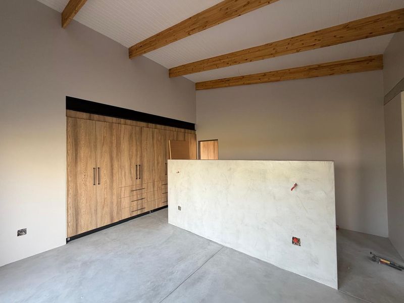 Spacious bedroom featuring exposed timber ceiling beams, polished concrete flooring, and extensive built-in wooden cabinetry with a central partition wall.