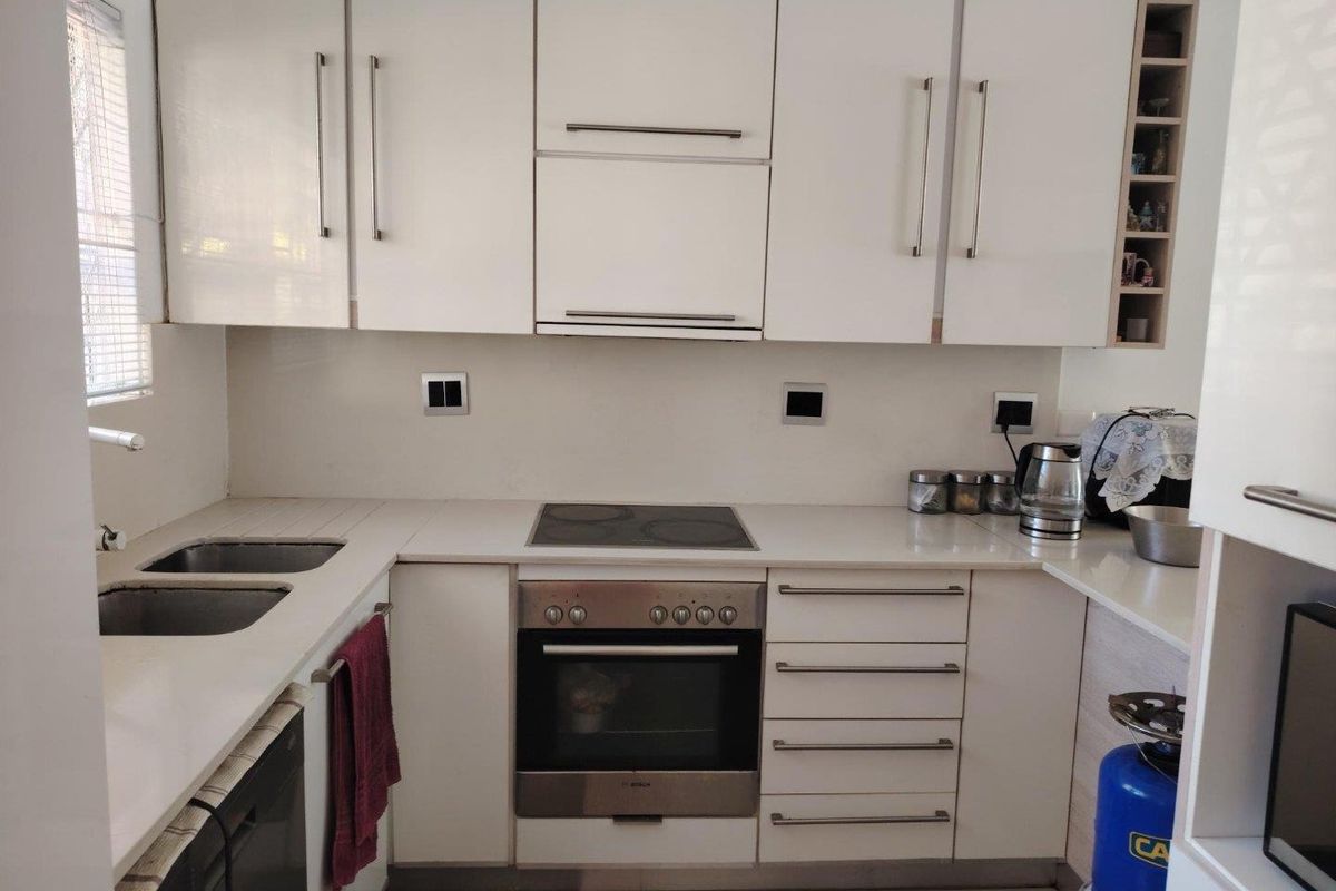 A functional kitchen featuring white cabinetry, stone countertops, a built-in oven, electric hob, and a double basin sink.