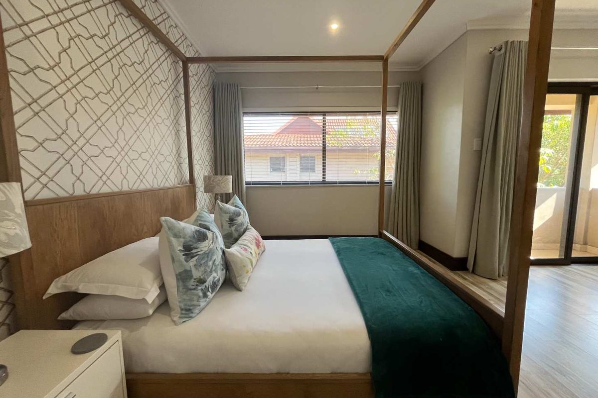 A well-lit bedroom featuring neutral wall finishes, tiled flooring, and a sliding door providing access to an outdoor balcony area.