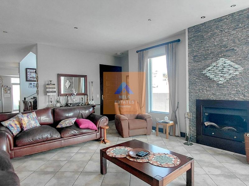 Spacious living room featuring a prominent stone-clad fireplace, neutral tiled flooring, and recessed downlighting, creating a warm and inviting atmosphere.