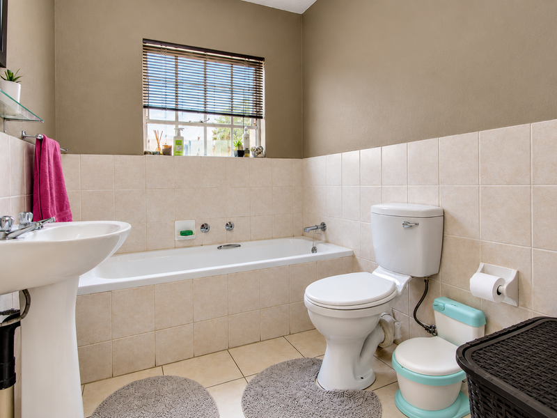 A functional bathroom featuring a pedestal washbasin, a built-in bathtub, and a toilet, finished with neutral ceramic wall and floor tiles.