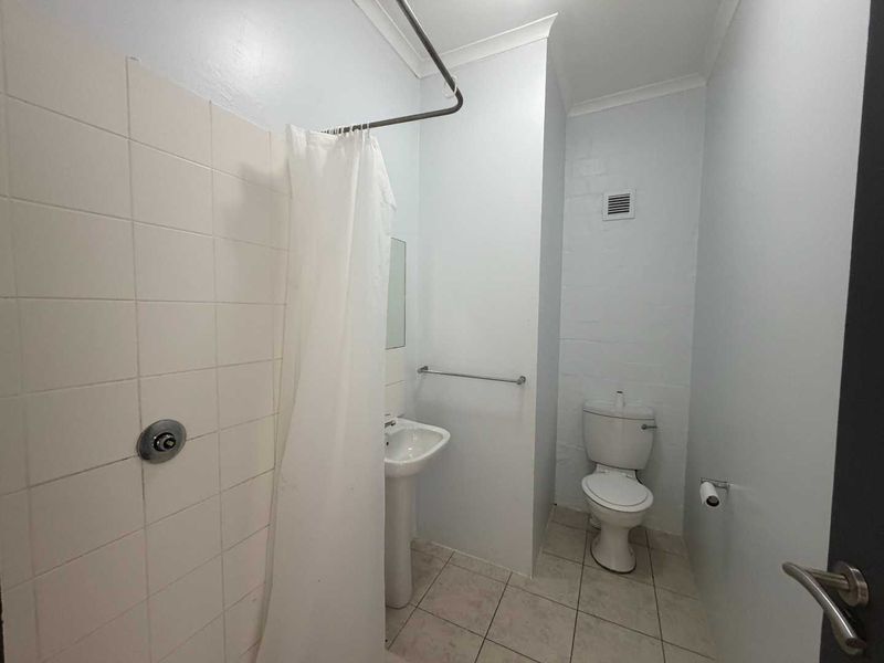 A functional bathroom featuring a pedestal sink, toilet, and a tiled shower area with a curtain rail.
