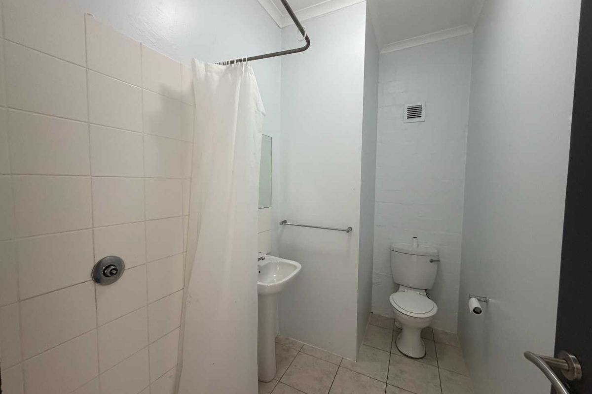 A functional bathroom featuring a pedestal sink, toilet, and a tiled shower area with a curtain rail.