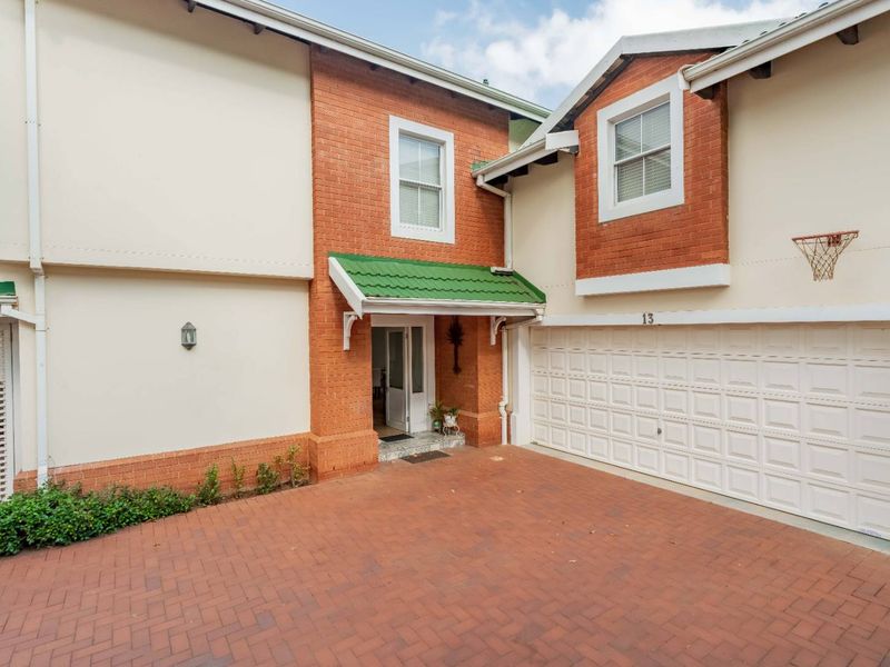 Front elevation of a townhouse featuring a brick driveway, double garage, and a covered entrance with a green tiled canopy.