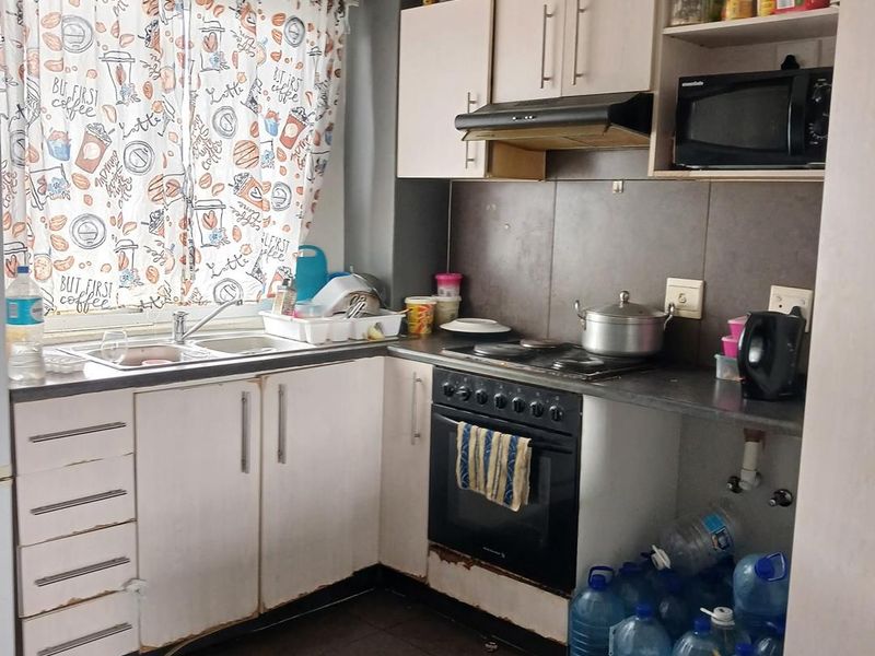 Compact kitchen featuring built-in cabinetry, electric hob, oven, extractor fan, and tiled splashback, requiring some cosmetic updates to the cabinetry.