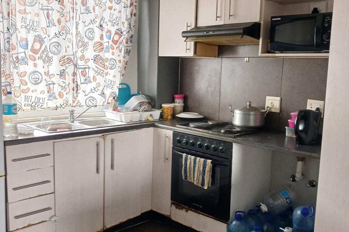 Compact kitchen featuring built-in cabinetry, electric hob, oven, extractor fan, and tiled splashback, requiring some cosmetic updates to the cabinetry.