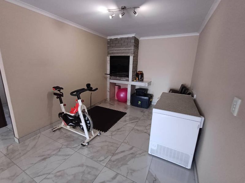 A multi-purpose room featuring tiled flooring and a built-in brick fireplace, currently utilized as a home gym and utility space.