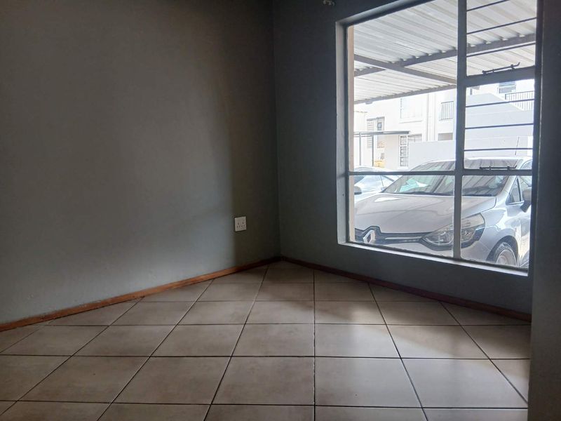 An empty living room featuring neutral tiled flooring and a large window with security bars, offering a blank canvas for personalization.