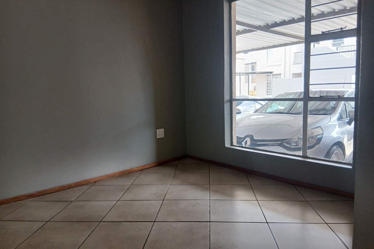 An empty living room featuring neutral tiled flooring and a large window with security bars, offering a blank canvas for personalization.