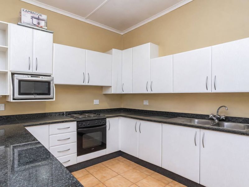 A functional kitchen featuring white cabinetry, dark granite countertops, a built-in oven, electric hob, and a stainless steel sink.