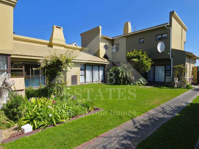 Rear view of the property featuring a well-maintained garden, paved pathway, and multiple sliding glass door access points to the main dwelling.
