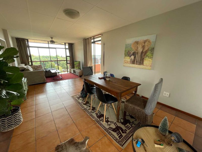 Open-plan living and dining area featuring tiled flooring, a ceiling fan, and large sliding glass doors providing access to a balcony with natural light.