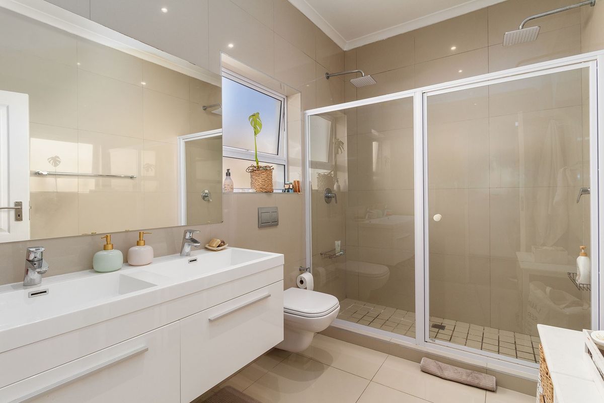Modern bathroom featuring a double vanity, wall-mounted toilet, and a spacious walk-in shower with a rain shower head and neutral tiled finishes.