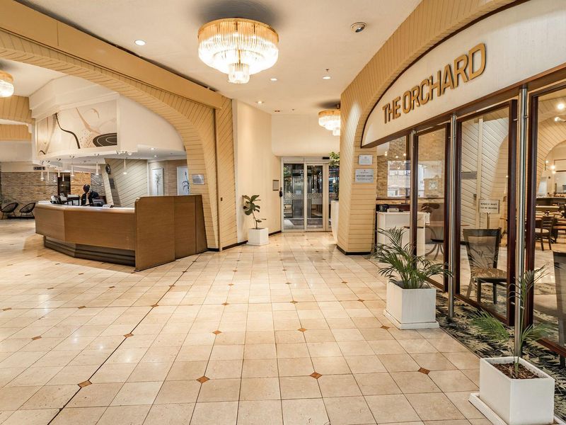 A spacious, well-lit clubhouse lobby featuring tiled flooring, decorative archways, chandeliers, and a reception desk, providing a welcoming entrance to the facility.