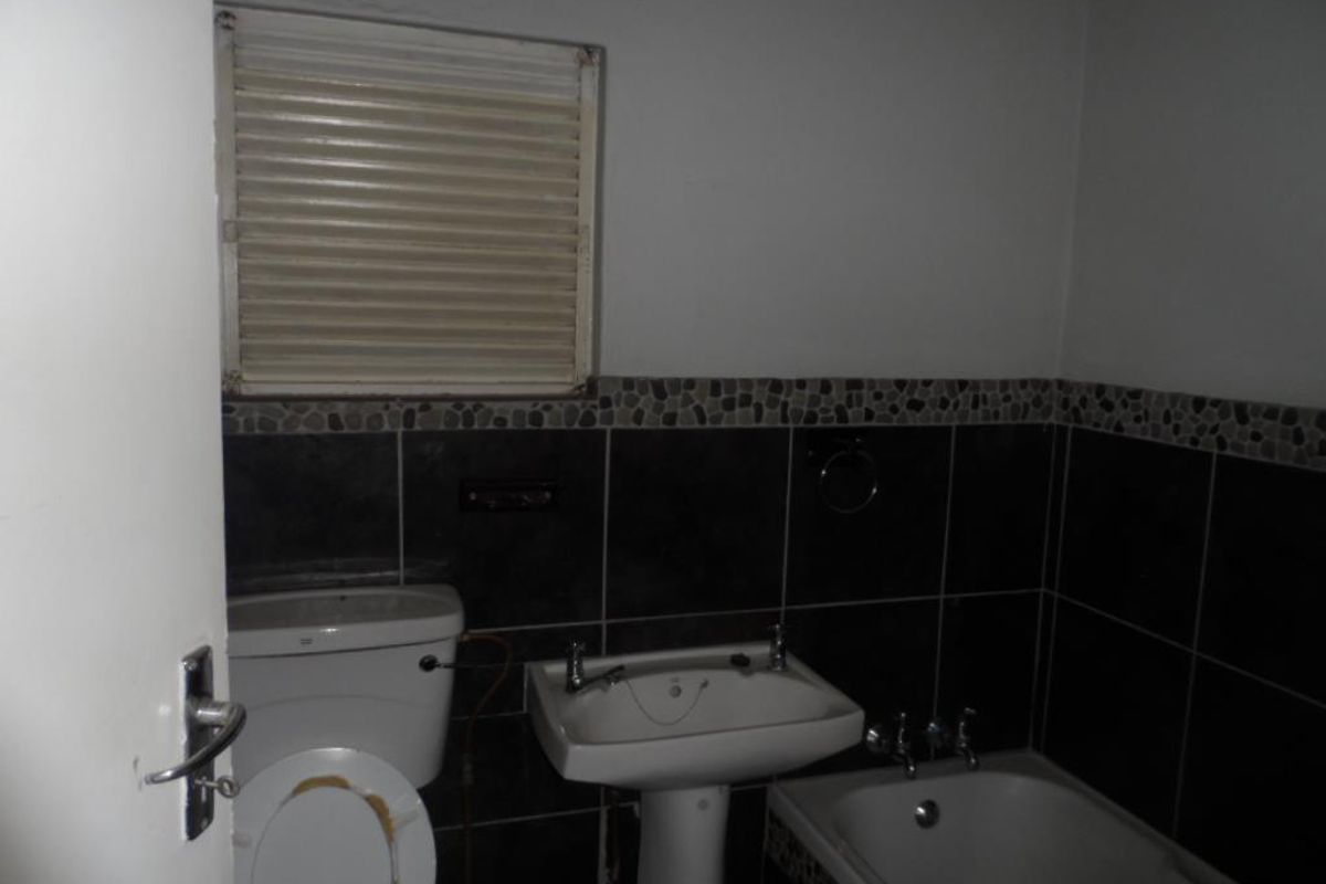 A compact bathroom featuring a pedestal basin, toilet, and bathtub with dark wall tiling and a window shutter.