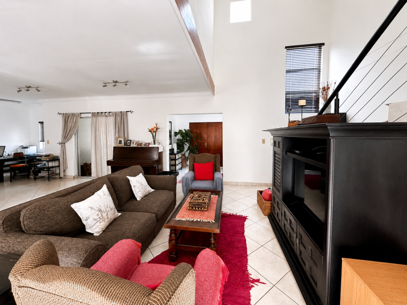 Spacious living room featuring double volume ceilings, exposed timber beams, tiled flooring, and a staircase with a modern railing.