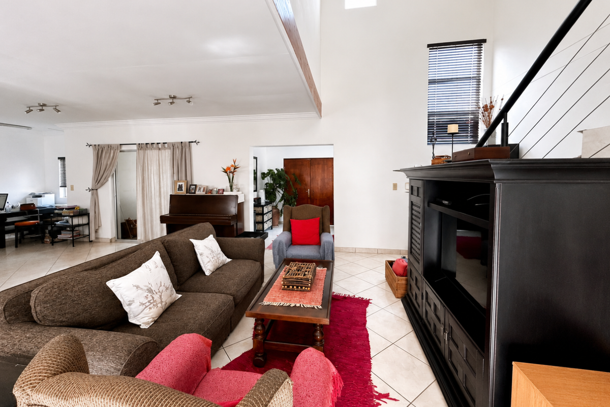 Spacious living room featuring double volume ceilings, exposed timber beams, tiled flooring, and a staircase with a modern railing.