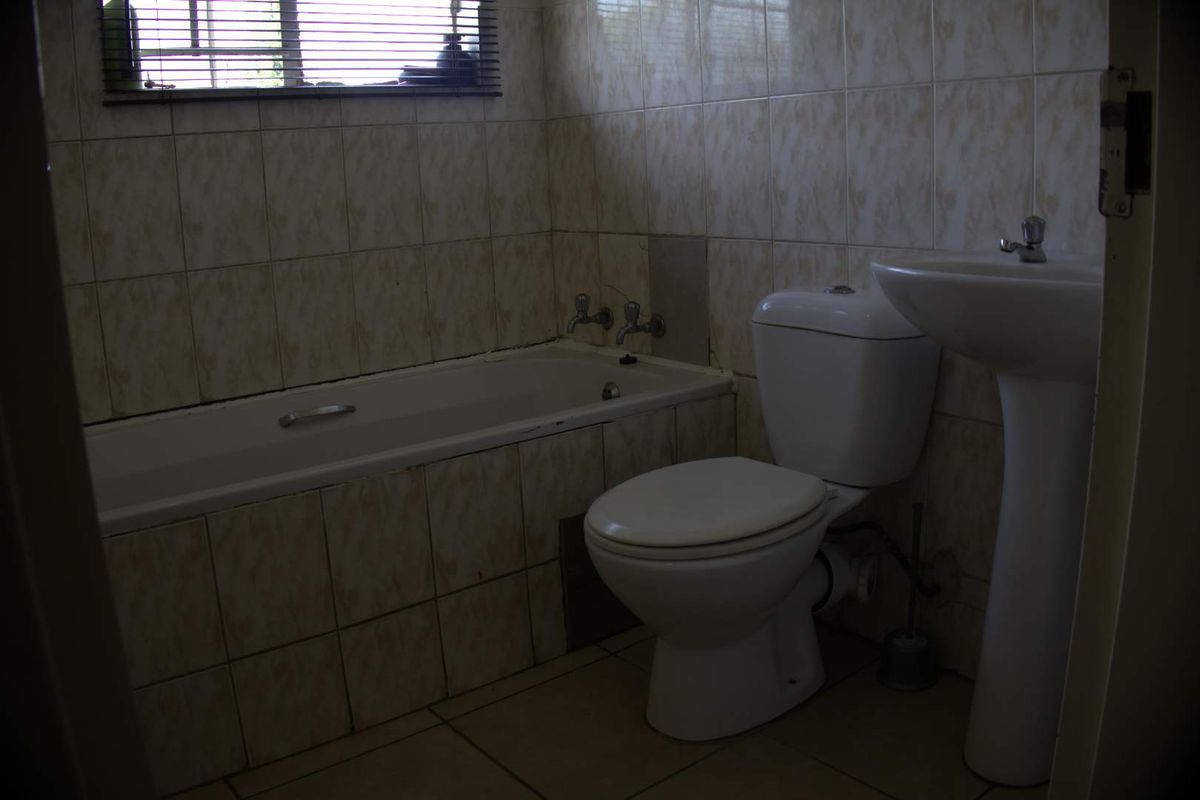 A dated bathroom featuring a standard bathtub, pedestal basin, and toilet with full-height wall tiling and a window with a venetian blind.