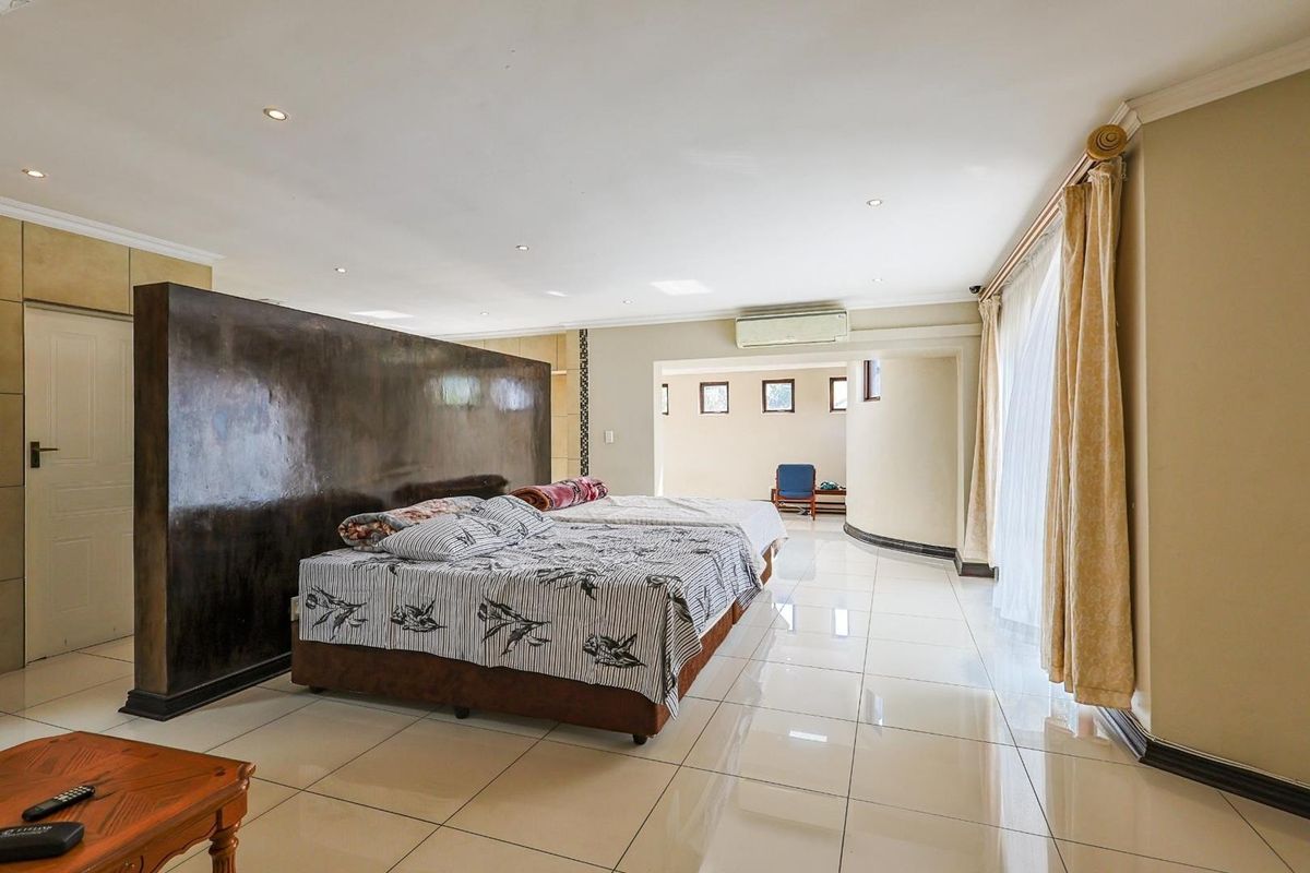 Spacious bedroom featuring large format floor tiles, a central room divider, recessed downlighting, and a wall-mounted air conditioning unit.