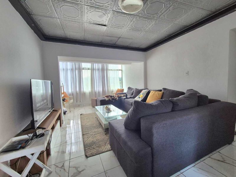 A living room featuring tiled flooring and a unique decorative ceiling, with large windows providing natural light.