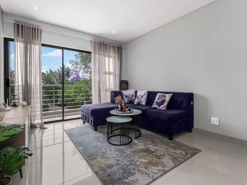A bright living room featuring large sliding glass doors that open onto a balcony, complemented by modern tiled flooring and recessed ceiling lighting.