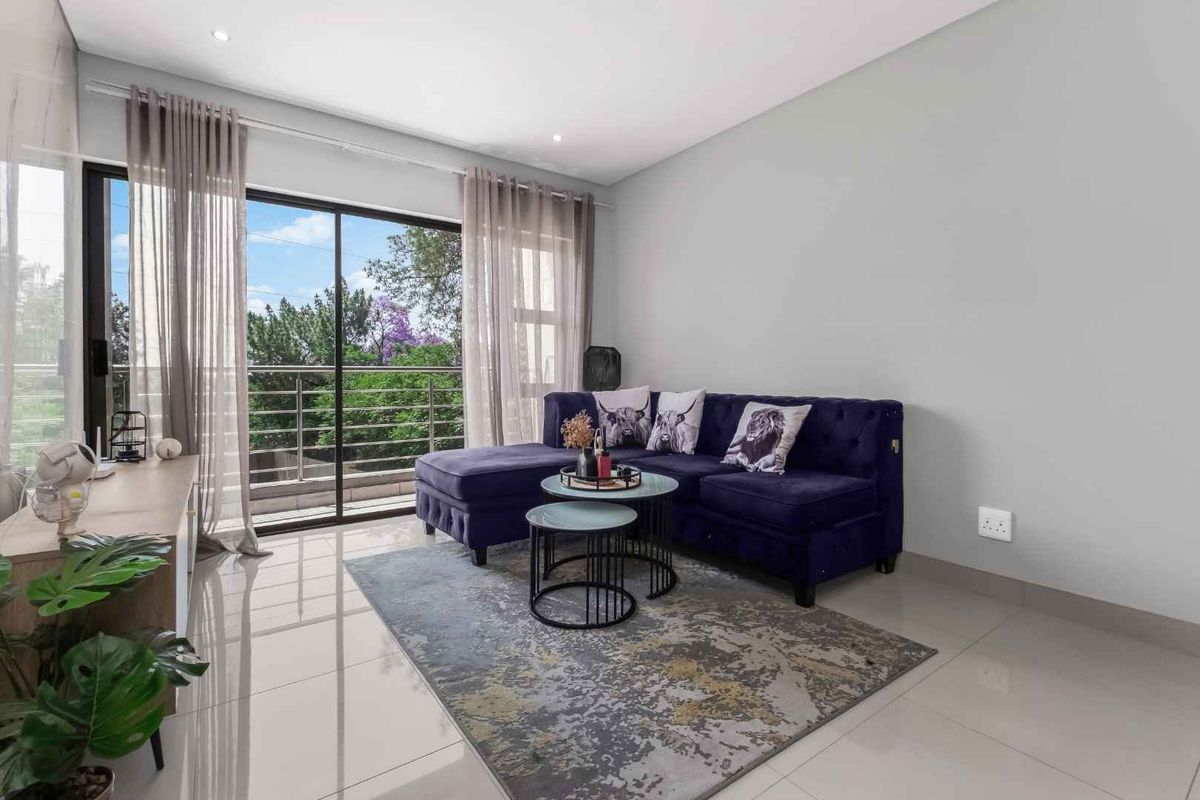 A bright living room featuring large sliding glass doors that open onto a balcony, complemented by modern tiled flooring and recessed ceiling lighting.