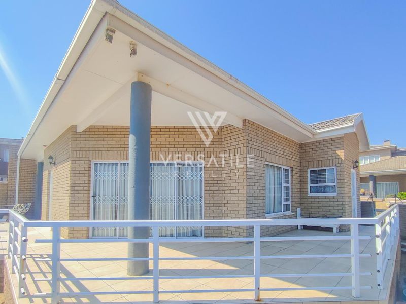A spacious covered patio featuring tiled flooring, a metal balustrade, and brick exterior walls, providing an ideal outdoor entertainment area for the townhouse.