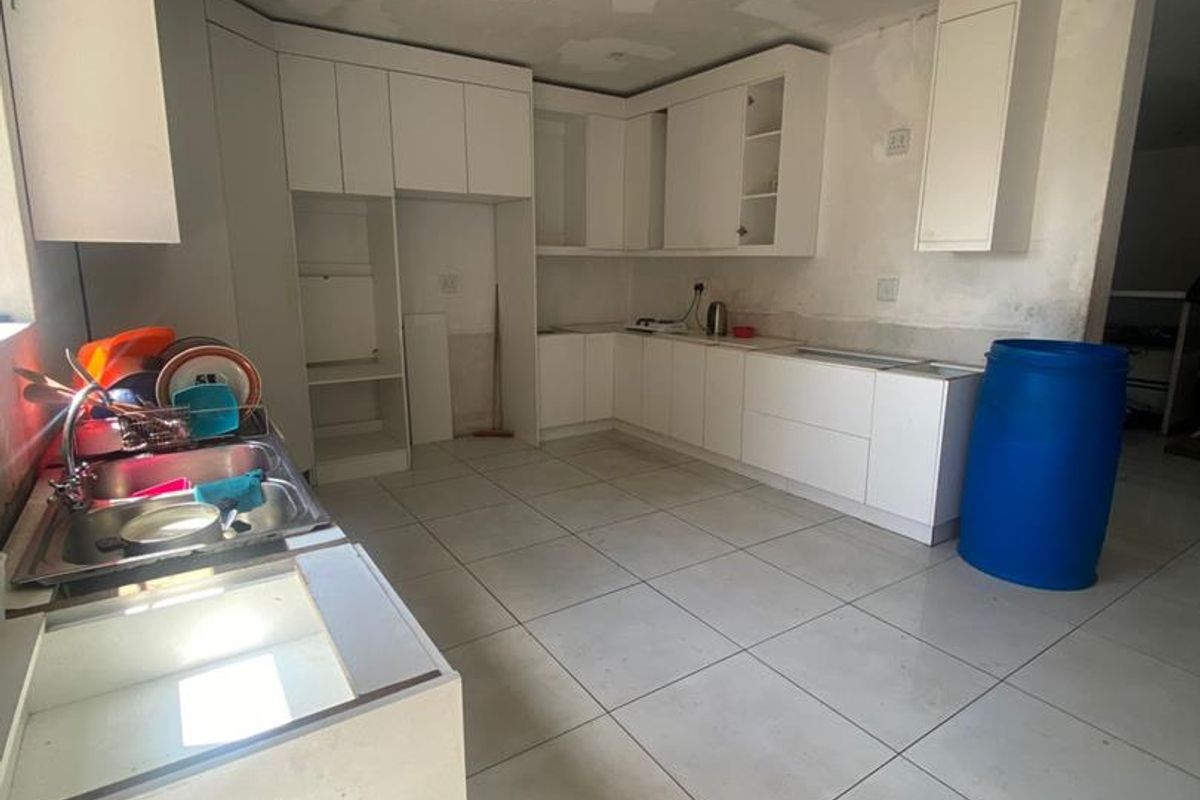 An unfinished kitchen space featuring white cabinetry, tiled flooring, and a stainless steel sink, currently undergoing renovation with incomplete ceiling and wall finishes.