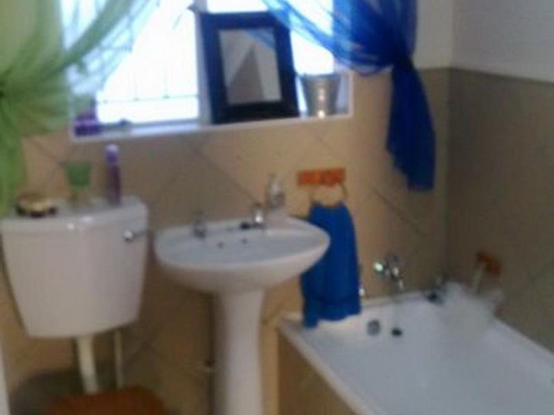 A functional bathroom featuring a pedestal washbasin, toilet, and bathtub with tiled finishes and a window with security bars.