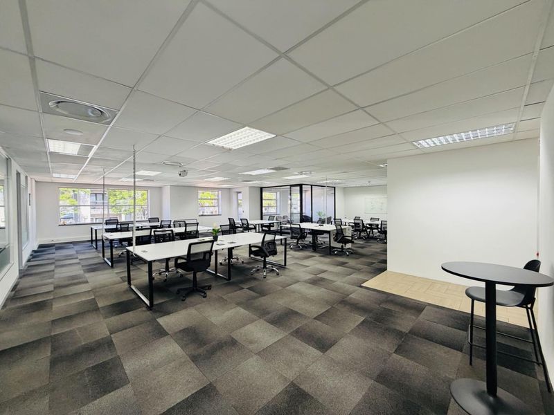 Spacious open-plan office area featuring suspended ceilings, recessed lighting, carpet tiles, and a glass-partitioned meeting room, providing a professional and functional workspace.