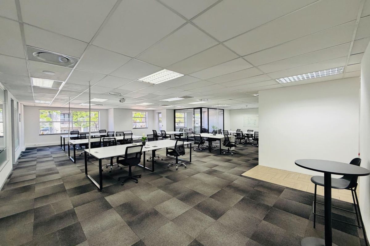 Spacious open-plan office area featuring suspended ceilings, recessed lighting, carpet tiles, and a glass-partitioned meeting room, providing a professional and functional workspace.