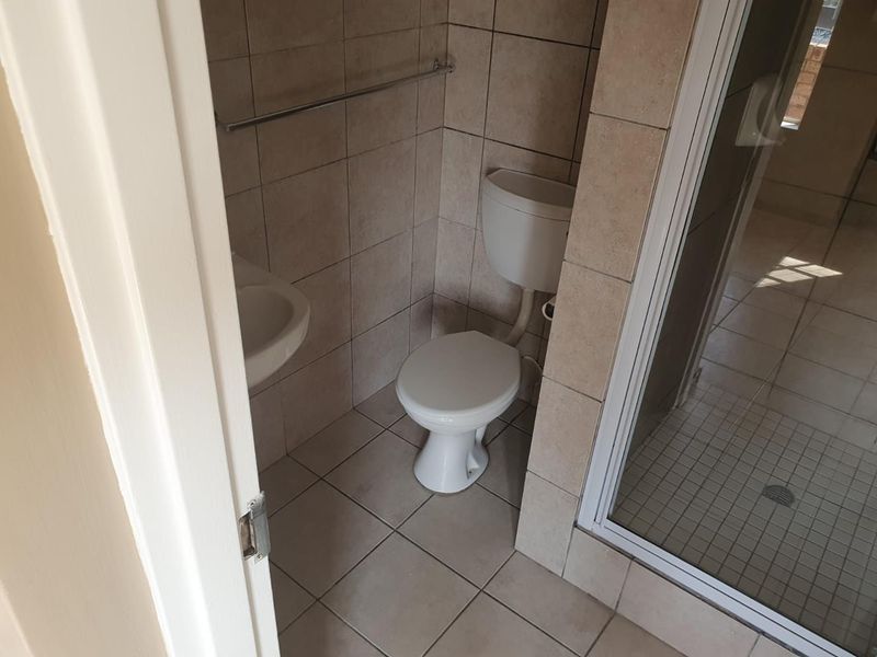 A functional bathroom featuring a toilet, wall-mounted basin, and a separate shower enclosure with neutral ceramic tiling throughout.