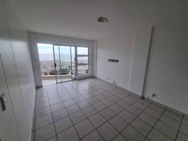 An empty, tiled living room featuring a sliding glass door that opens onto a balcony with ocean views.
