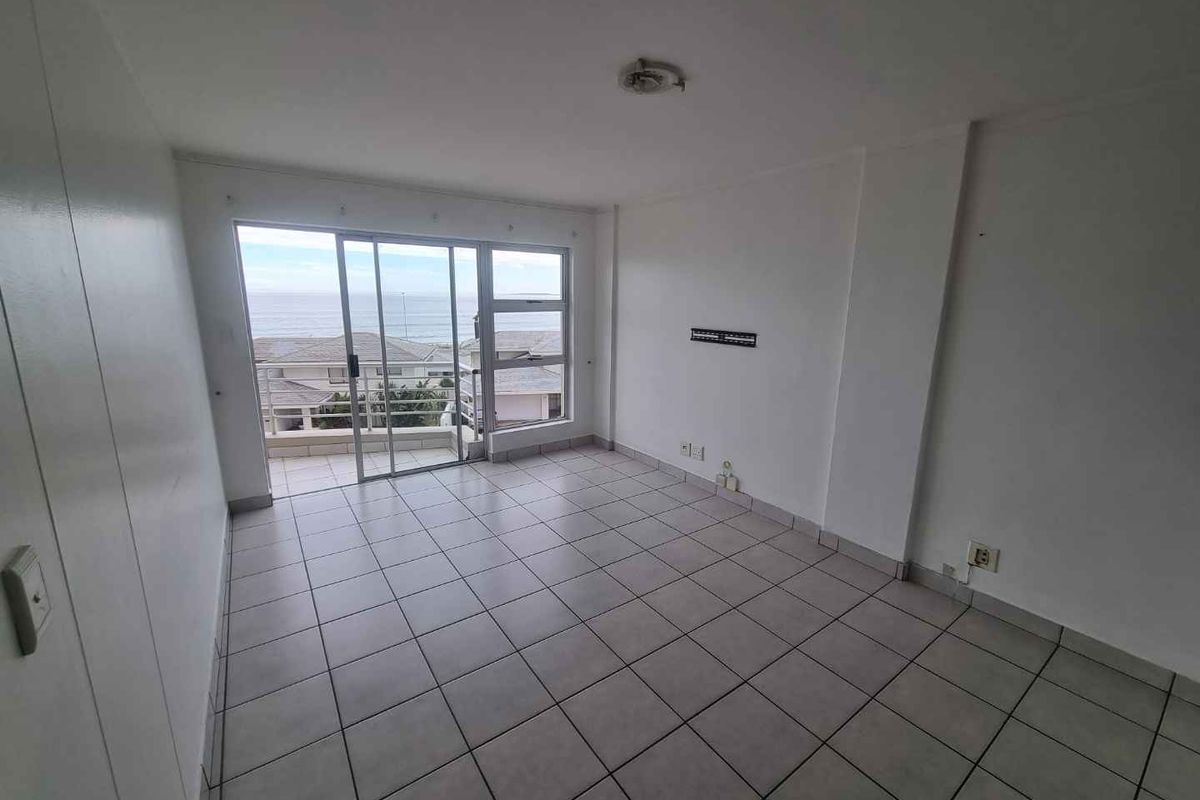 An empty, tiled living room featuring a sliding glass door that opens onto a balcony with ocean views.