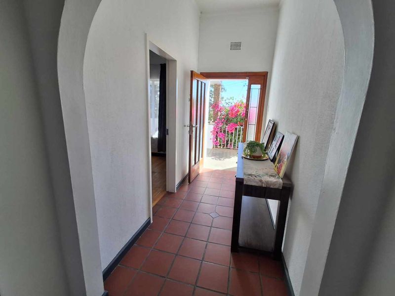 A bright hallway featuring terracotta floor tiles and an arched entryway leading to an outdoor patio area.