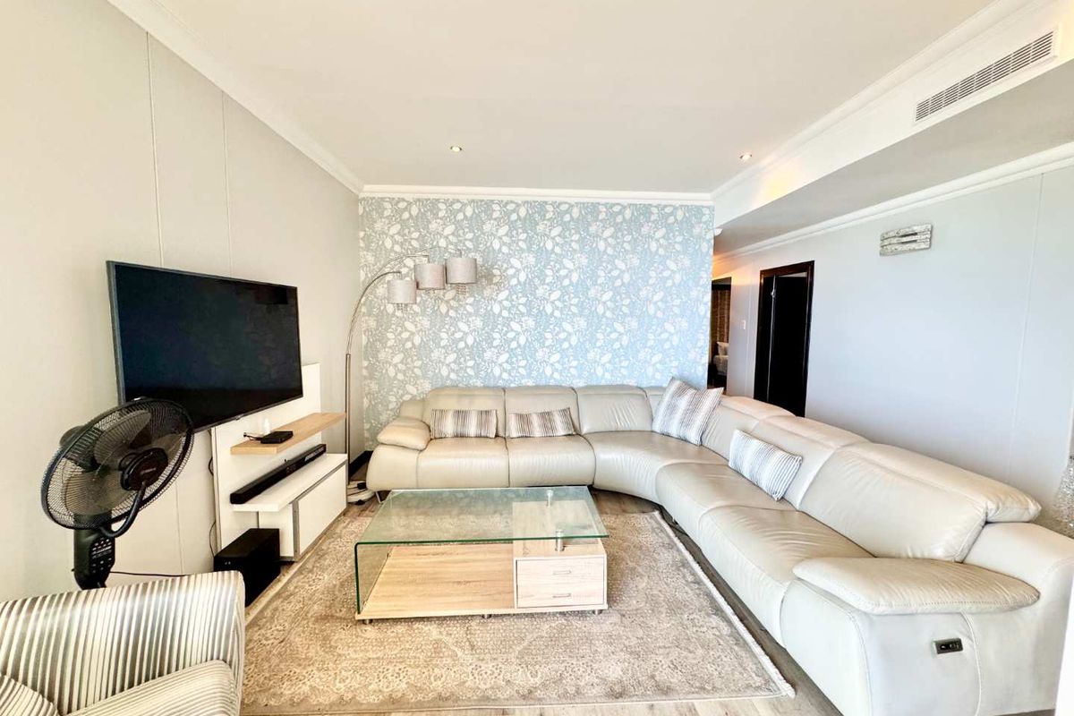 A bright and spacious living room featuring modern wood-look flooring, recessed ceiling lighting, and a decorative floral accent wall.