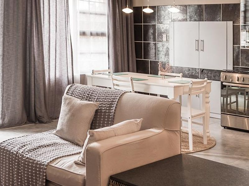 An open-plan living and kitchen area featuring tiled flooring, a modern stainless steel stove, and a dark tiled kitchen backsplash.