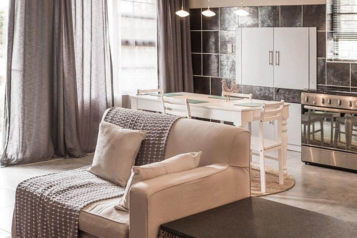 An open-plan living and kitchen area featuring tiled flooring, a modern stainless steel stove, and a dark tiled kitchen backsplash.