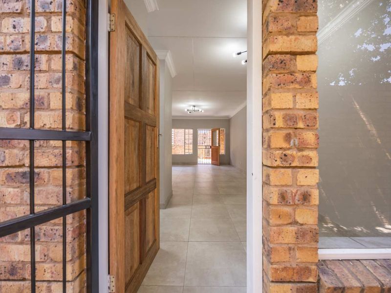 View from the entrance into an open-plan living area featuring neutral tiled flooring, exposed brick accents, and a secure gated entry.