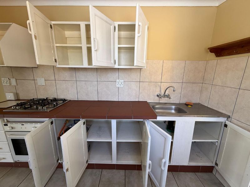 A dated kitchen featuring white cabinetry, a tiled countertop, gas hob, and built-in oven, offering a functional layout ready for modernization.