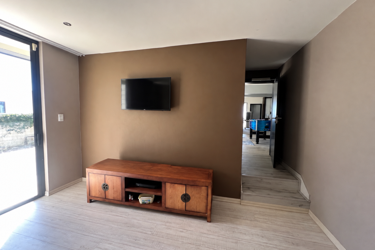 A living room featuring laminate flooring, recessed downlights, and a large sliding glass door providing natural light, with a view into an adjacent room.