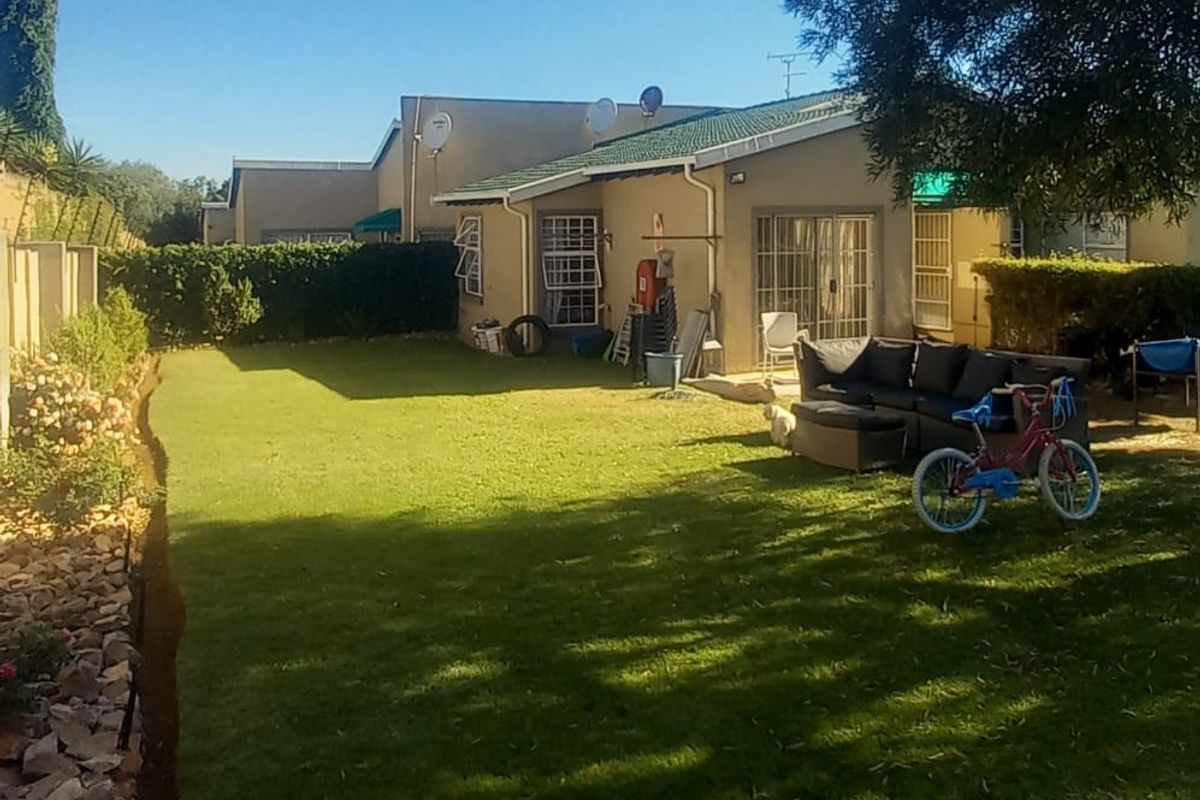 A private rear garden featuring a well-maintained lawn, boundary wall, and direct access to the townhouse via sliding glass doors.