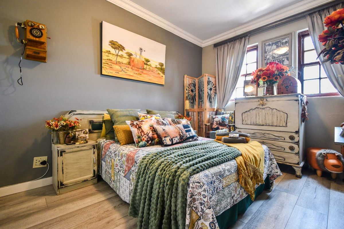 A cozy bedroom featuring wood-look laminate flooring, crown molding, and large windows that provide natural light.