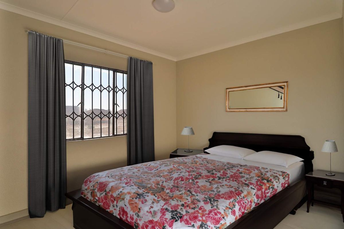 A functional bedroom featuring tiled flooring, coving, and a window fitted with security bars.