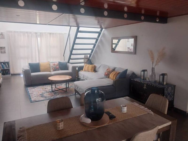 Spacious open-plan living and dining area featuring a modern metal staircase, timber-clad ceiling, and neutral tiled flooring.